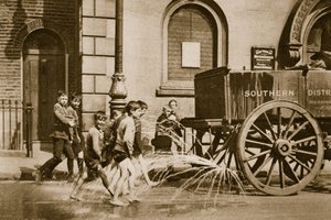 East End children cooling themselves from a water-cart during a heat wave by English Photographer